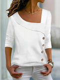 Femme portant un haut blanc asymétrique à manches trois-quarts avec boutons décoratifs, style décontracté chic, collier doré, cheveux bouclés.