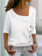 Femme portant un haut blanc asymétrique à manches trois-quarts avec boutons décoratifs, style décontracté chic, collier doré, cheveux bouclés.