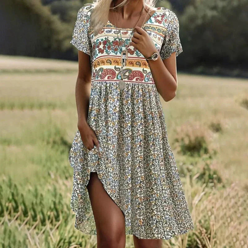 Robe d'été bohème à motifs floraux et ethniques, manches courtes, col rond, portée par une femme dans un champ verdoyant. Mode féminine tendance.