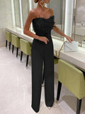 Combinaison noire élégante avec plumes, femme tenant un sac à main blanc, intérieur moderne avec chaises vertes, ambiance chic et sophistiquée.
