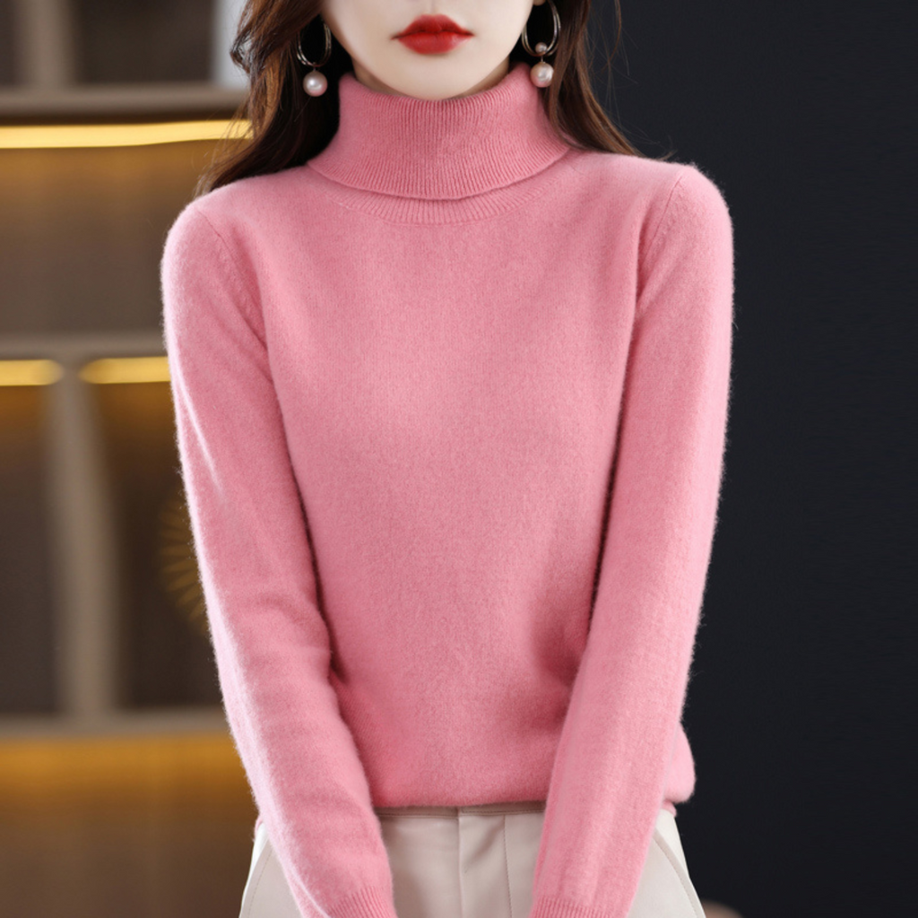 Femme portant un pull rose en cachemire à col roulé, élégante et moderne, idéal pour la mode automne-hiver. Accessoires: boucles d'oreilles perles.