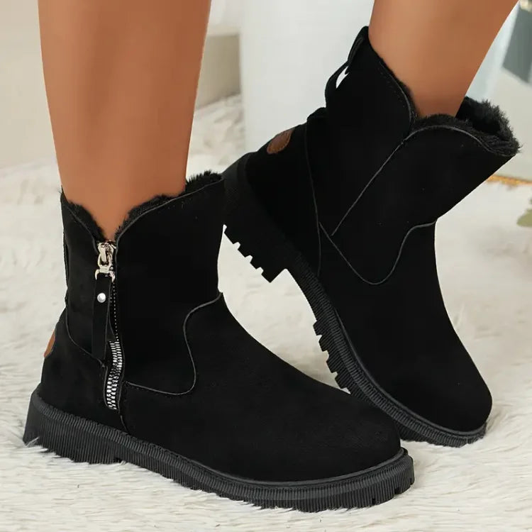 Bottes noires en daim avec fermeture éclair latérale et doublure en fourrure, portées sur un tapis blanc. Chaussures d'hiver élégantes et confortables.