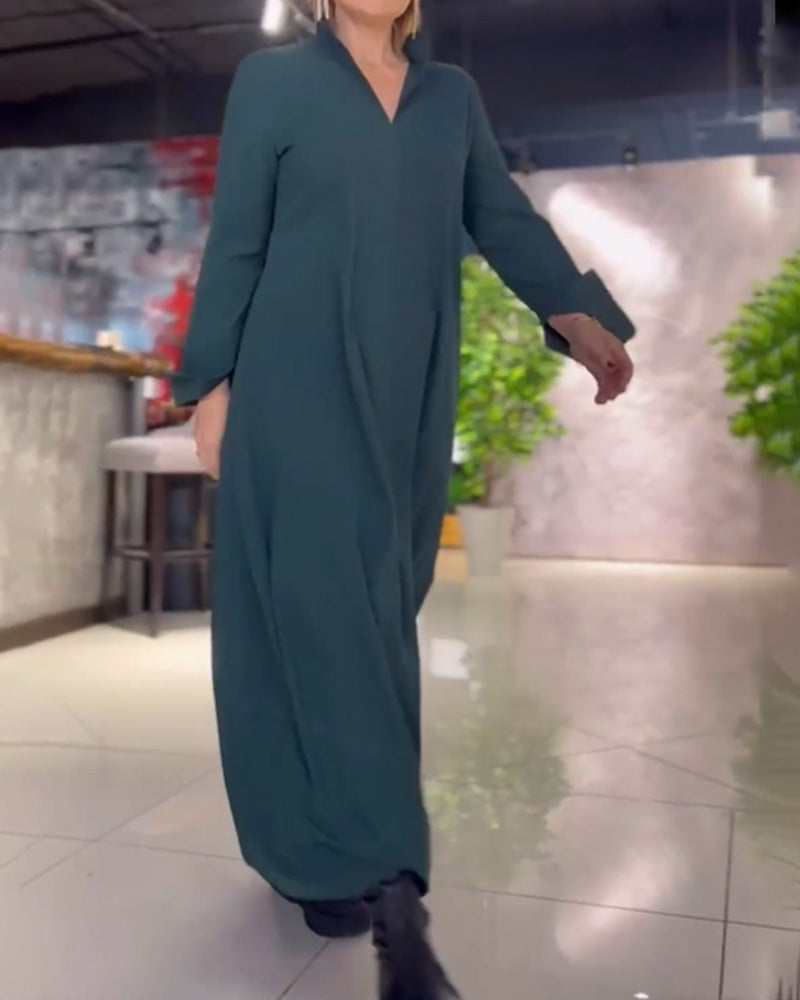 Femme portant une robe longue verte, marchant dans un intérieur moderne avec plantes et murs texturés. Mode élégante, tenue décontractée chic.