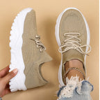 Chaussures de sport beiges en maille avec semelles blanches épaisses, tenues par une main, sur fond beige. Mode tendance, baskets confortables.