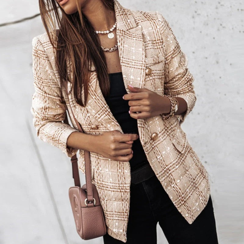 Femme portant un blazer à carreaux beige élégant, sac à main rose, collier perles, bracelet doré, mode automne chic, style urbain tendance.