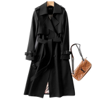 Trench-coat noir élégant avec ceinture, boutons et détails classiques, accompagné d'un sac à main marron en cuir matelassé. Mode automne chic.