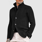 Homme portant un cardigan noir élégant avec boutons, col relevé, sur chemise noire et pantalon beige. Mode masculine chic et moderne.
