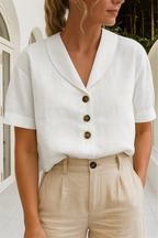 Femme portant une chemise blanche en lin avec col en V et boutons marron, associée à un pantalon beige, dans un cadre élégant et lumineux.