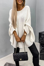 Femme portant un pull blanc ample, pantalon noir et sac à main matelassé noir. Mode automne-hiver, style chic et décontracté.