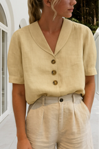 Femme portant une chemise beige en lin avec col en V et boutons marron, assortie à un pantalon beige, dans un cadre moderne et lumineux.