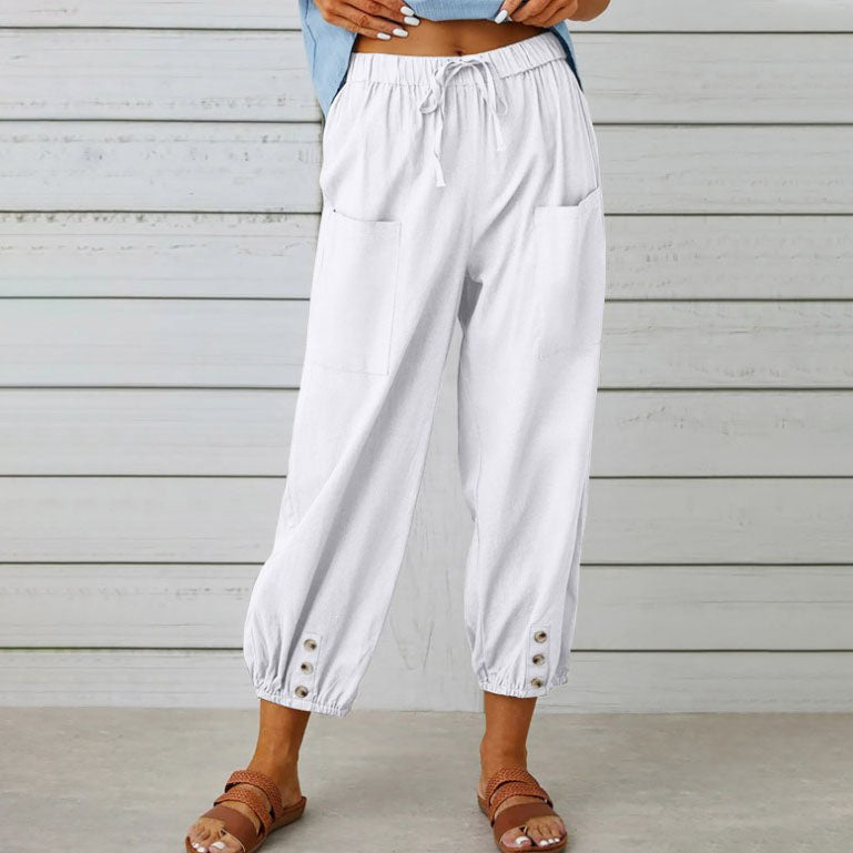 Pantalon blanc ample pour femme avec poches avant, boutons décoratifs en bas, style décontracté, idéal pour l'été, fond en bois clair.