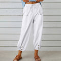 Pantalon blanc ample pour femme avec poches avant, boutons décoratifs en bas, style décontracté, idéal pour l'été, fond en bois clair.
