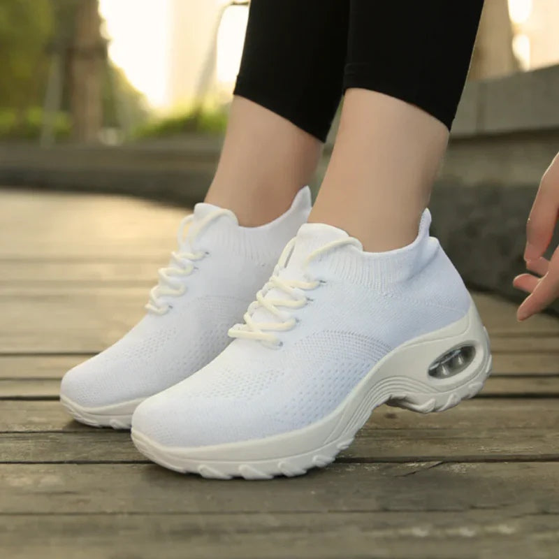 Chaussures de sport blanches pour femme sur plancher en bois, design moderne avec semelle épaisse, idéales pour la course et le fitness.