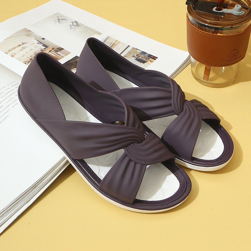 Sandales violettes élégantes sur fond jaune, posées sur un livre ouvert, avec un gobelet transparent à couvercle marron à côté. Mode estivale tendance.