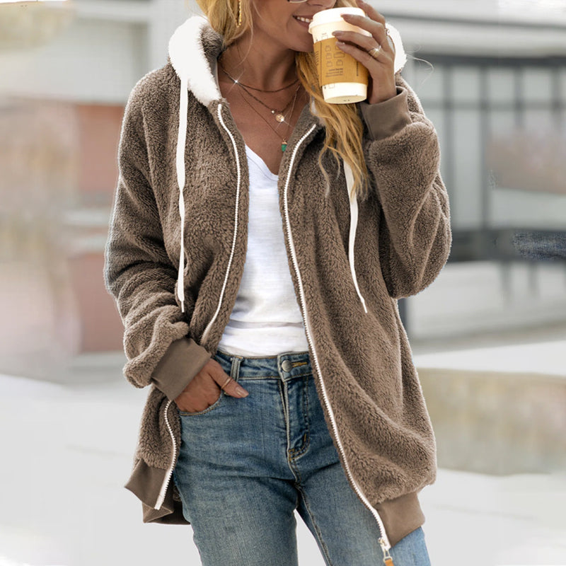 Femme portant une veste en polaire marron avec capuche blanche, tenant un gobelet de café. Mode décontractée, tenue automne-hiver, style urbain.