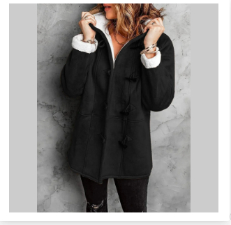 Femme portant un manteau noir à capuche avec doublure blanche, posant contre un mur gris. Mode hiver, style élégant, vêtements chauds.