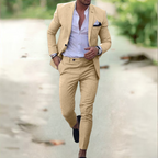 Homme en costume beige élégant, chemise blanche ouverte, marchant en extérieur. Mode masculine, style chic, tenue décontractée.