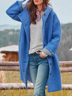 Femme portant un manteau bleu en laine, écharpe colorée, pull gris et jeans, posant en extérieur. Mode automne-hiver, style décontracté.