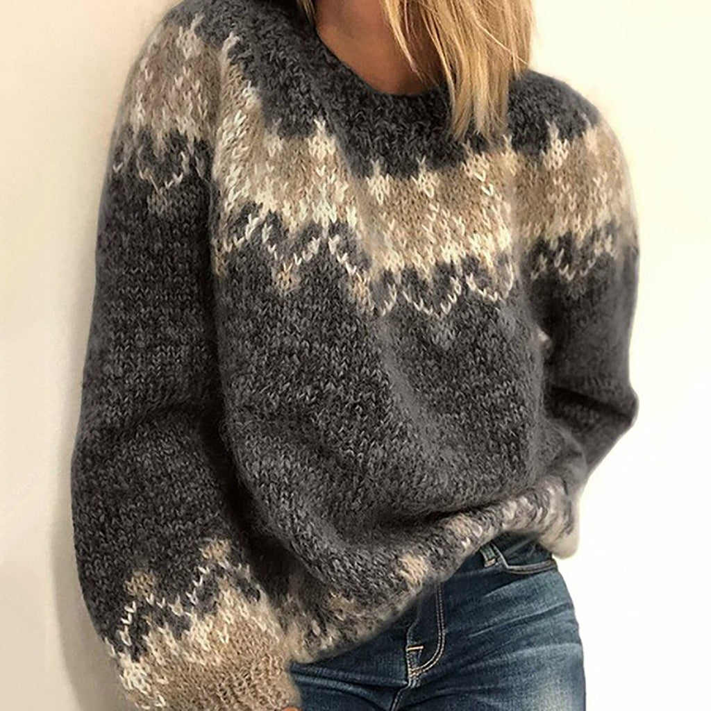 Femme portant un pull en laine épais gris à motifs géométriques, manches longues, col rond, associé à un jean bleu. Mode hiver tendance.