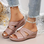 Sandales roses confortables pour femmes, avec talon compensé et détails perforés, portées avec un jean décontracté et bracelet de cheville perlé.