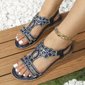 Sandales ornées de strass bleus et argentés sur pieds féminins, posées sur une terrasse en bois, avec bracelet chaîne doré. Mode estivale élégante.