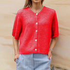 Femme portant un cardigan rouge vif à boutons blancs, manches courtes, avec un pantalon à carreaux bleus. Mode féminine élégante et colorée.