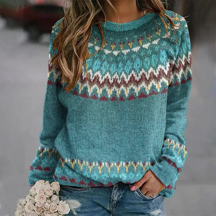 Femme portant un pull bleu à motifs nordiques, tenant un bouquet de fleurs blanches. Mode automne-hiver, style décontracté et tendance.