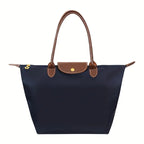 Sac à main en toile bleu marine avec poignées en cuir marron, design élégant et pratique, idéal pour le quotidien et les voyages.