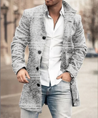 Homme portant un manteau gris texturé, chemise blanche et jean décontracté, marchant en ville. Mode masculine élégante, style urbain chic.