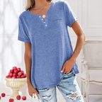 Femme portant un t-shirt bleu à boutons, jeans déchirés, posant près d'un vase de pommes rouges. Mode décontractée, style estival.