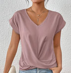 Femme portant un t-shirt rose à col en V, manches courtes, avec collier doré, posant devant un mur blanc. Mode féminine décontractée, style chic.