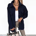 Femme portant une veste noire élégante, chemise blanche, pantalon beige, collier doré, tenant un sac à main à carreaux. Mode chic et moderne.