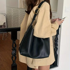 Femme portant un grand sac à main noir en cuir, tenue beige, intérieur moderne. Mode féminine élégante, accessoires tendance.