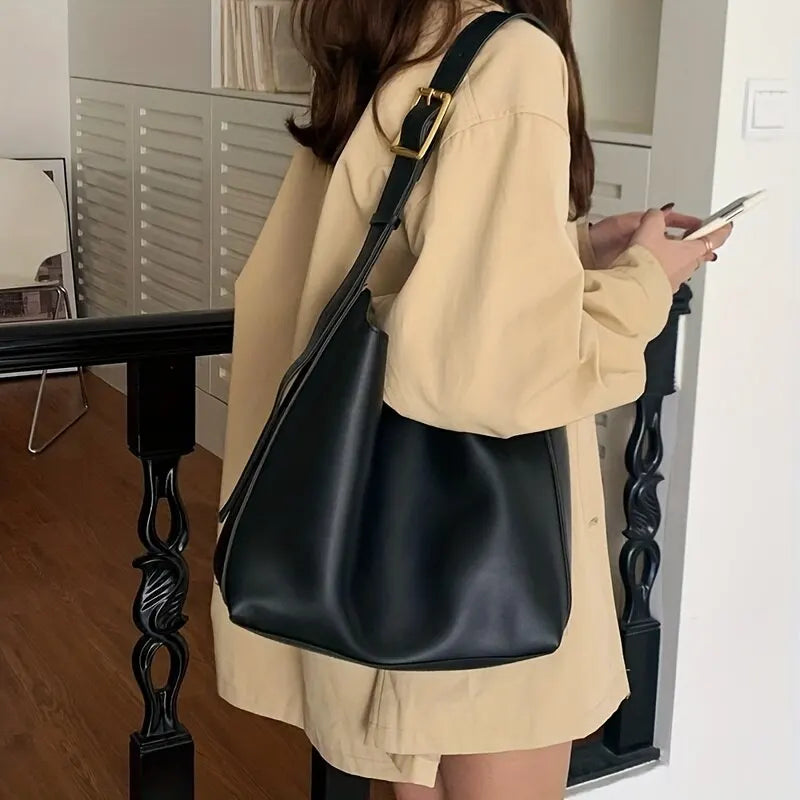 Femme portant un grand sac à main noir en cuir, tenue beige, intérieur moderne. Mode féminine élégante, accessoires tendance.