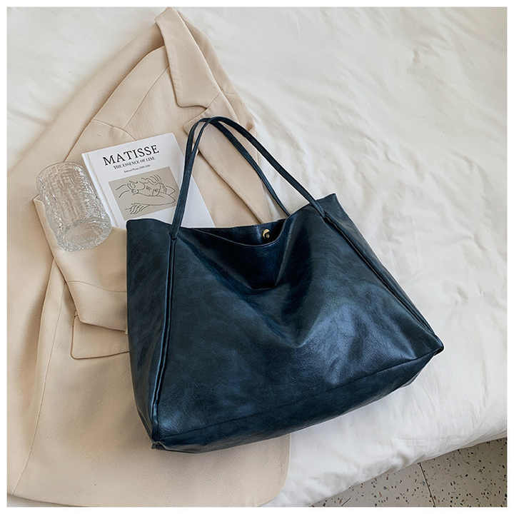 Sac à main en cuir noir sur un lit, accompagné d'un magazine d'art "Matisse", un manteau beige et un verre transparent. Accessoire mode élégant.