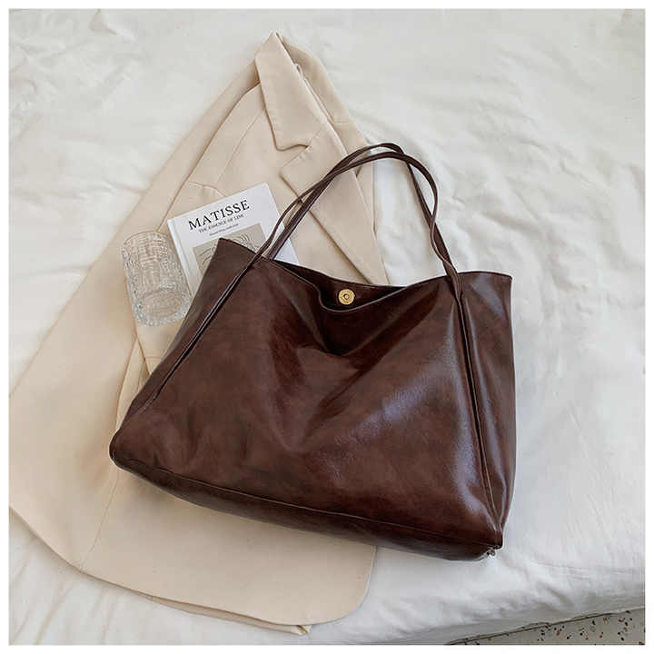 Sac à main en cuir marron sur un manteau beige, avec un livre "Matisse" et un verre transparent. Accessoire mode élégant et tendance.