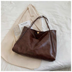 Sac à main en cuir marron sur un manteau beige, avec un livre "Matisse" et un verre transparent. Accessoire mode élégant et tendance.