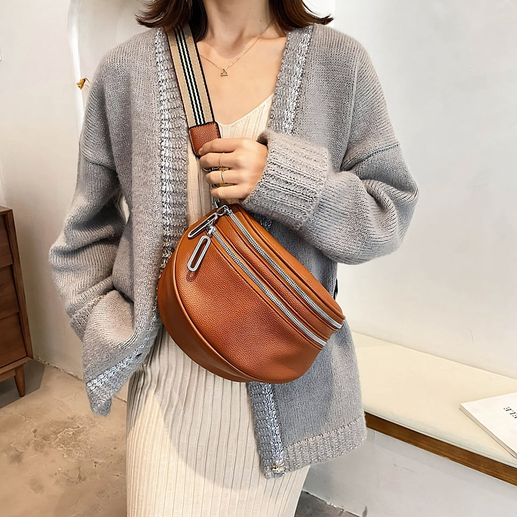 Femme portant un cardigan gris et une robe beige, tenant un sac banane en cuir marron avec bandoulière rayée. Mode automne, accessoires tendance.