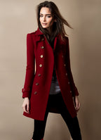 Femme portant un manteau rouge élégant avec boutons dorés, posant sur fond beige. Mode automne-hiver, style chic et tendance.
