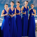 Cinq femmes en robes bleues élégantes, tenant des flûtes de champagne, posent devant un paysage côtier ensoleillé. Mariage, élégance, robes de soirée.