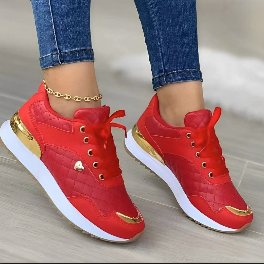 Chaussures de sport rouges pour femme avec détails dorés, semelle blanche, portées avec un jean. Sneakers tendance, mode féminine, style urbain.