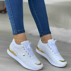 Baskets blanches et dorées pour femme, portées avec un jean bleu. Chaussures de sport élégantes, tendance et modernes.