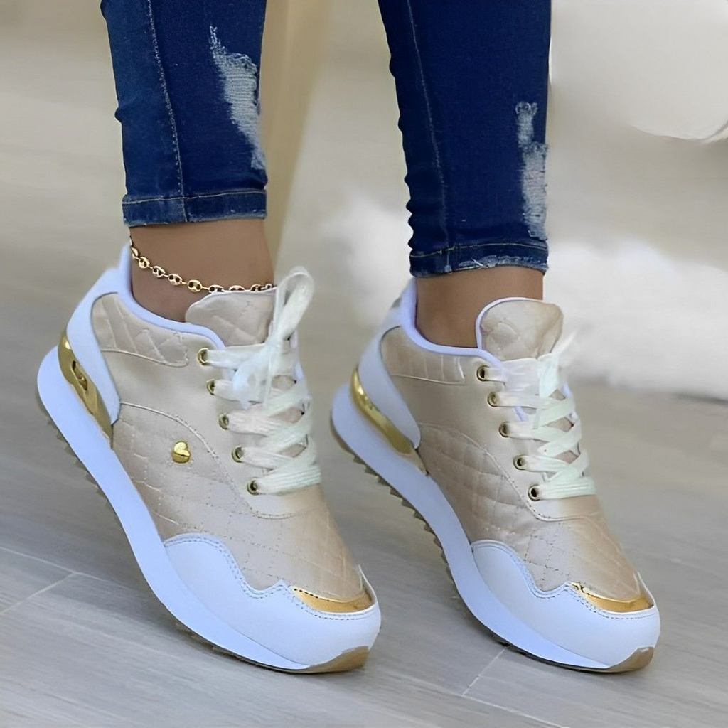 Chaussures de sport dorées pour femme avec détails blancs et dorés, portées avec un jean déchiré. Style moderne et tendance, parfait pour la mode urbaine.