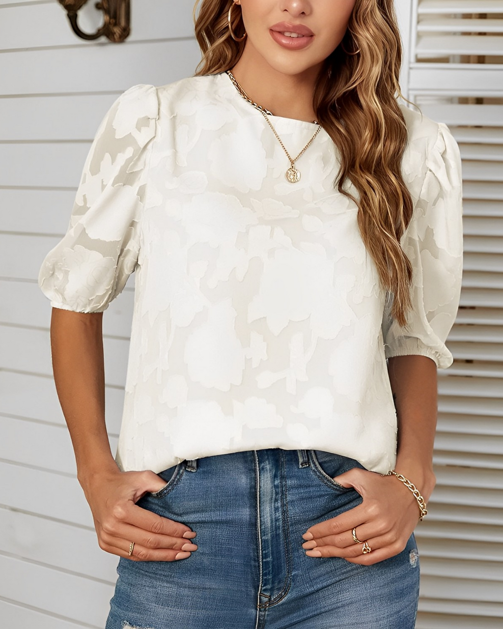 Femme portant un chemisier blanc à motifs floraux et manches bouffantes, associée à un jean bleu. Mode féminine élégante et décontractée.