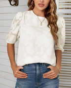 Femme portant un chemisier blanc à motifs floraux et manches bouffantes, associée à un jean bleu. Mode féminine élégante et décontractée.