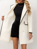 Femme portant un manteau blanc élégant avec bordures noires, robe noire moulante, cheveux ondulés, sur fond blanc. Mode chic automne-hiver.