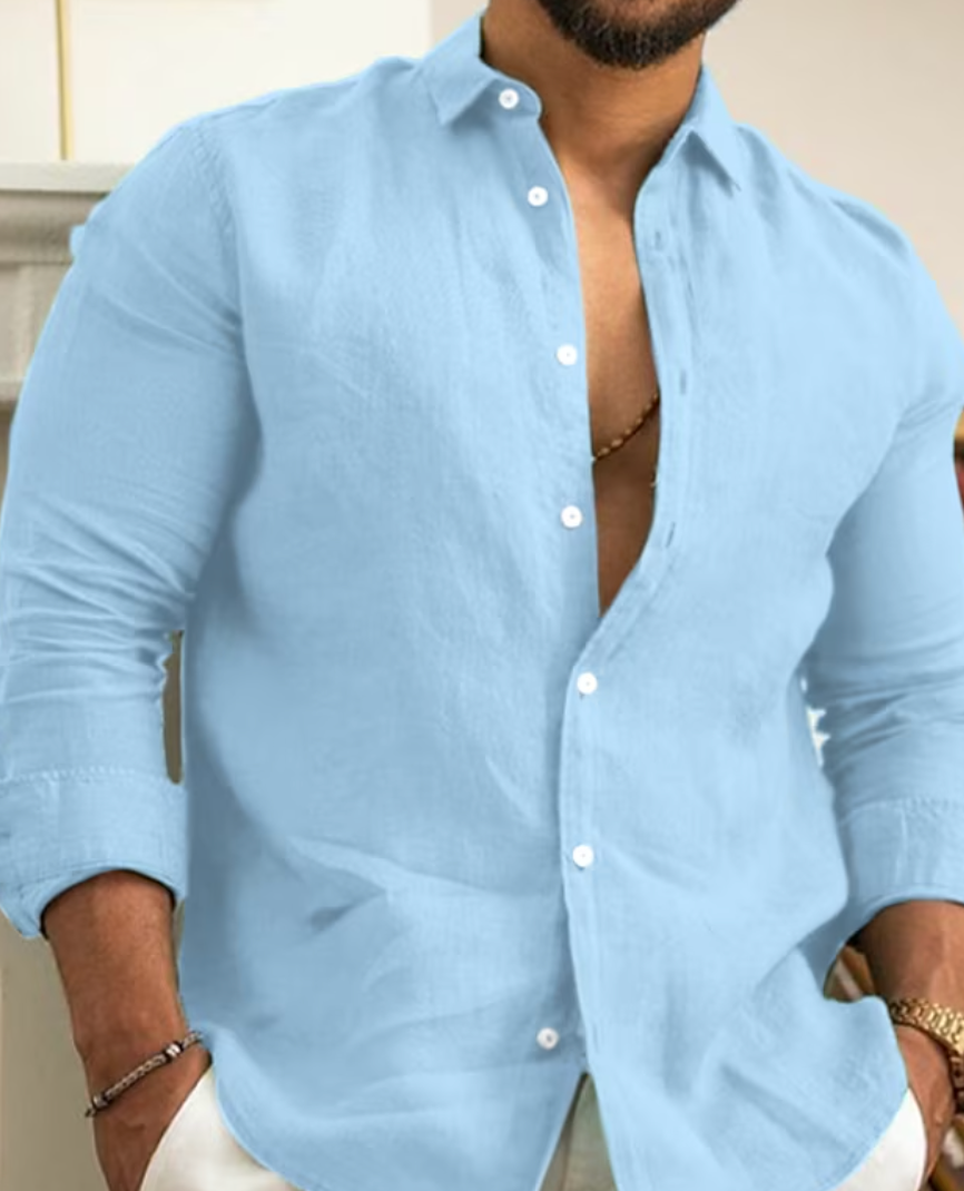 Homme portant une chemise en lin bleu clair, manches retroussées, col ouvert, posant avec les mains dans les poches. Mode masculine élégante.