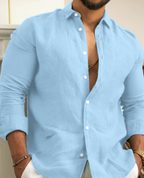 Homme portant une chemise en lin bleu clair, manches retroussées, col ouvert, posant avec les mains dans les poches. Mode masculine élégante.