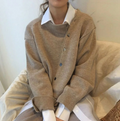 Femme portant un pull beige en laine avec chemise blanche, assise sur un canapé. Mode automne-hiver, style décontracté et élégant.