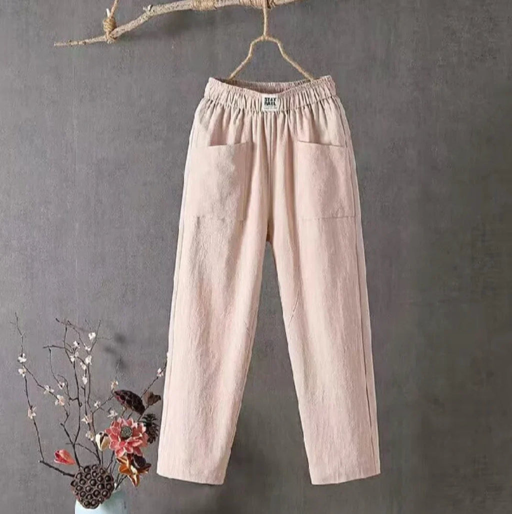 Pantalon en lin beige suspendu, style décontracté, avec poches avant. Décor floral en bas à gauche. Mode minimaliste, tendance et confortable.